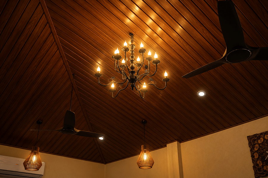 A brass chandelier hanging from a dark, vaulted wooden ceiling lit by warm pendant lamps at The Garud Forest, Tadoba