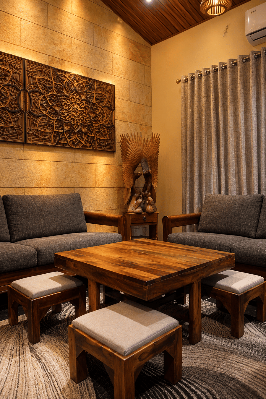 A lounge with grey sofa seating, a low wooden table, and carved mandala panels on a stone wall at The Garud Forest, Tadoba