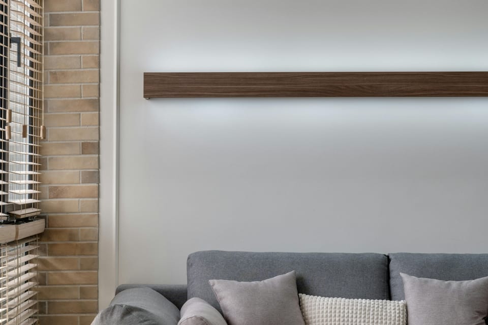 A living area with a grey sofa, multiple cushions, a round gold-legged coffee table, and a wall-mounted split air-conditioning unit above.