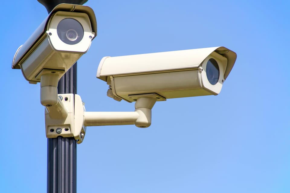 2 outdoor CCTV security cameras mounted on a pole against a clear blue sky.