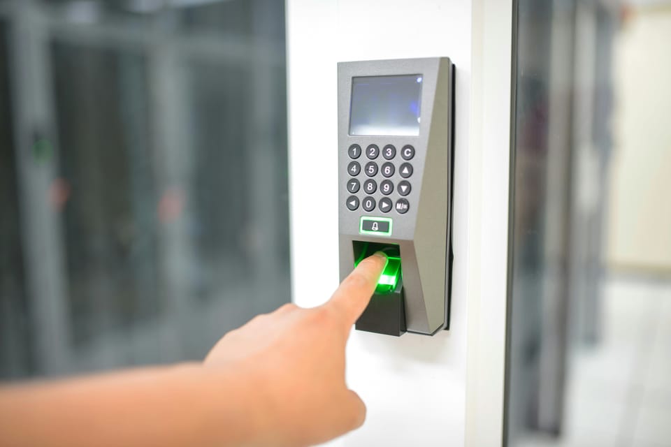 A close-up of a finger pressing the biometric fingerprint scanner on a digital keypad door access panel.