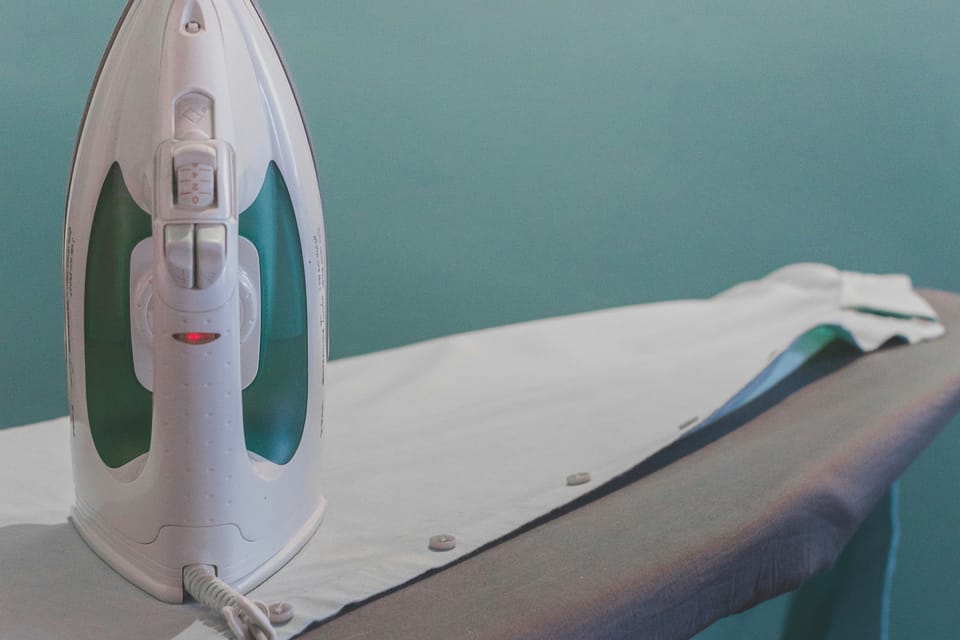 A close-up of an electric iron resting upright on a fabric-covered ironing board with a shirt laid out beside it.
