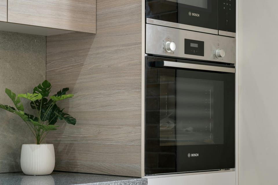 A section of a kitchenette with a built-in Bosch microwave stacked above a built-in Bosch oven, wooden cabinetry, and a small potted plant on the counter.