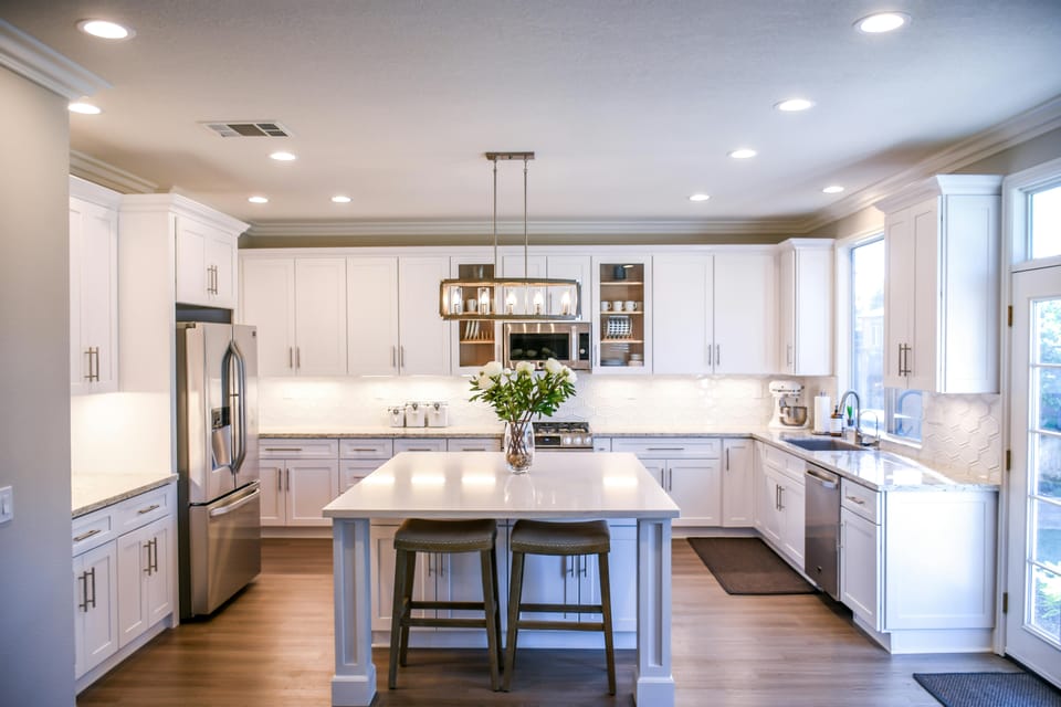 Pendant lights over the island seating for two in the white modular kitchen at Wabi-Sabi, Juhu, with a stainless steel refrigerator to the side.