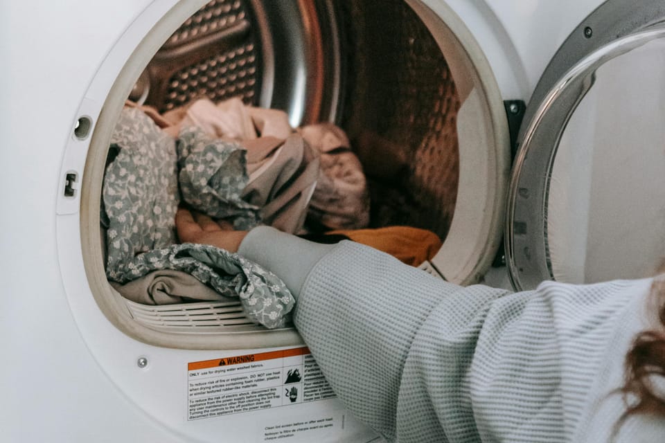 A close-up of a person hands loading clothes into the open drum of a front-loading washing machine or dryer.