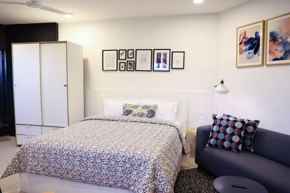 Bedroom at Wabi-Sabi, Juhu, with a patterned bedspread, a white wardrobe, a gallery wall of framed prints, and a navy sofa with printed cushions.