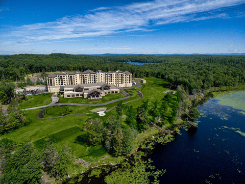 YO1 Longevity & Health Resorts in Catskills surrounded by green trees and a dark lake under a blue sky