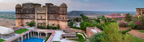 Facade view of  Tijara Fort-Palace - 19th Century, Alwar with a swimming pool in the foreground.