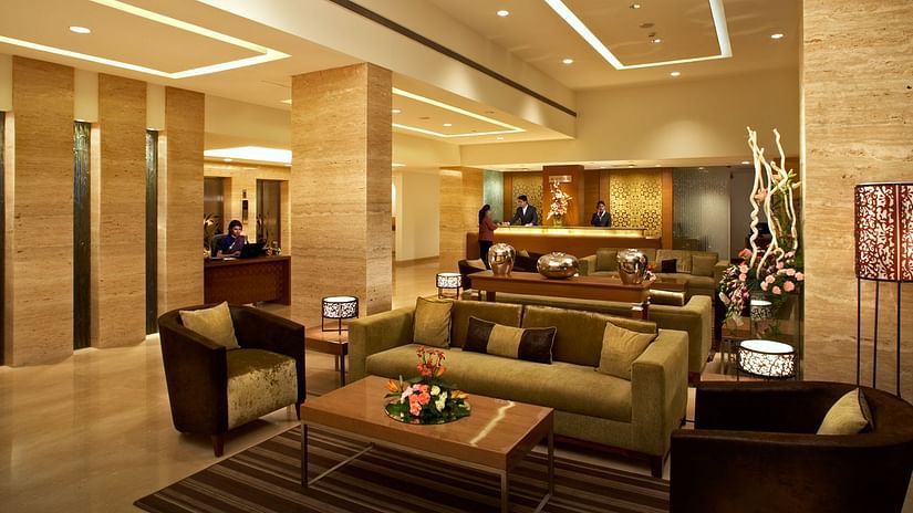 An image of a reception lobby featuring sofa sets, centre table, reception desks, and a few people standing at Adarsh Hamilton