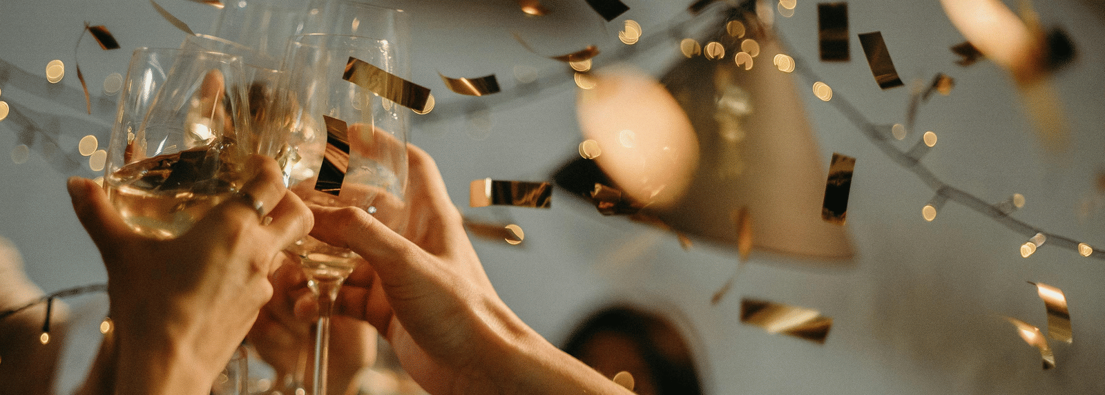 Group of people raising champagne glasses in a toast amid golden confetti at a festive celebration.