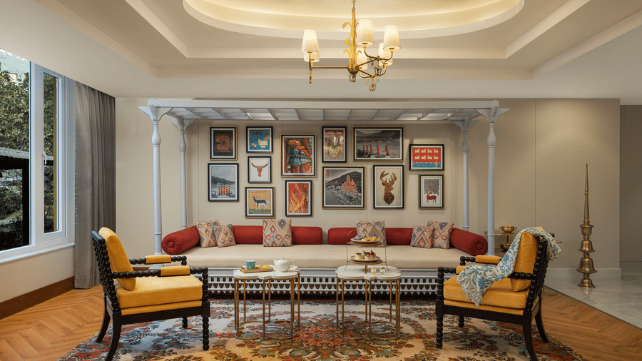 Elegant living room at Aloha on the Ganges Resort with sectional sofa, red and beige cushions, framed artwork wall, yellow armchairs, chandelier, and patterned rug.