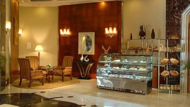 Elegant and cosy Chai Bar at The Manohar, Hyderabad, showcasing a bakery display, plush corner seating, and warm ambient lighting with floor lamps