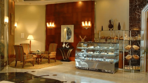 Elegant and cosy Chai Bar at The Manohar, Hyderabad, showcasing a bakery display, plush corner seating, and warm ambient lighting with floor lamps