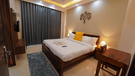 Bedroom of Lime Tree Hotels & Service Apartment Private Limited featuring a grey throw, yellow cushions, and a wooden side table.