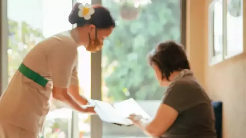 Spa therapist offering a foot treatment to a seated woman by a window, with candles and spa items nearby. at Karma Chalets