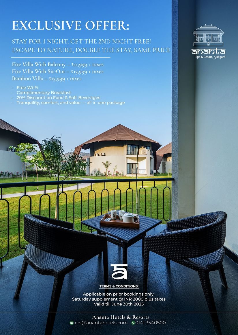 A balcony with a table and two chairs overlooks lawns and villa-style buildings under a clear sky. Text above highlights an exclusive hotel offer. Hotel and contact details appear at the bottom