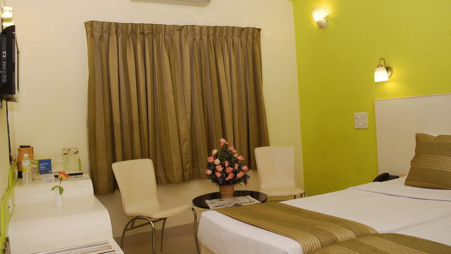 Hotel room interior featuring adjoined twin beds with olive green throws, a light green accent wall, and a vanity area - Hotel Pandian