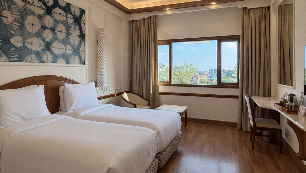 Twin beds with patterned bases are arranged under a ceiling fan and recessed lighting in the Deluxe Twin room at Clarks Amer, Jaipur.