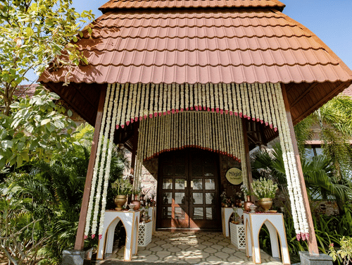 A roof supported by white pillars, adorned with flower vases and flower garlands hanging from the top, leading to an inviting door