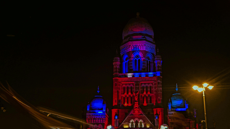 The illuminated facade of Chhatrapati Shivaji Maharaj Terminus at night, with light trails from passing traffic.