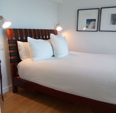 Bed with white linens and wooden headboard at Casa Morada, shown from a side angle.