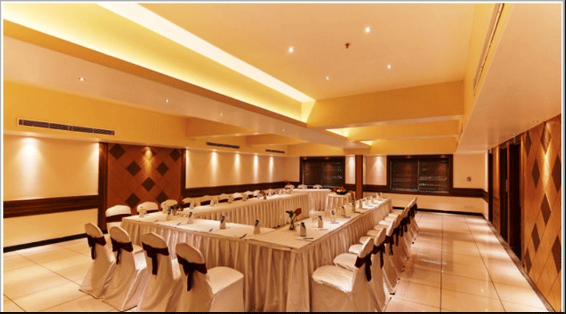 Banquet hall with arranged tables and chairs, ceiling lights, and wooden wall panels.