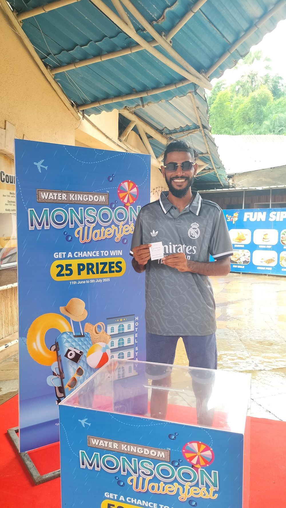 Water Kingdom Monsoon Waterfest winner smiling while holding a gift, standing in front of the event's vibrant backdrop