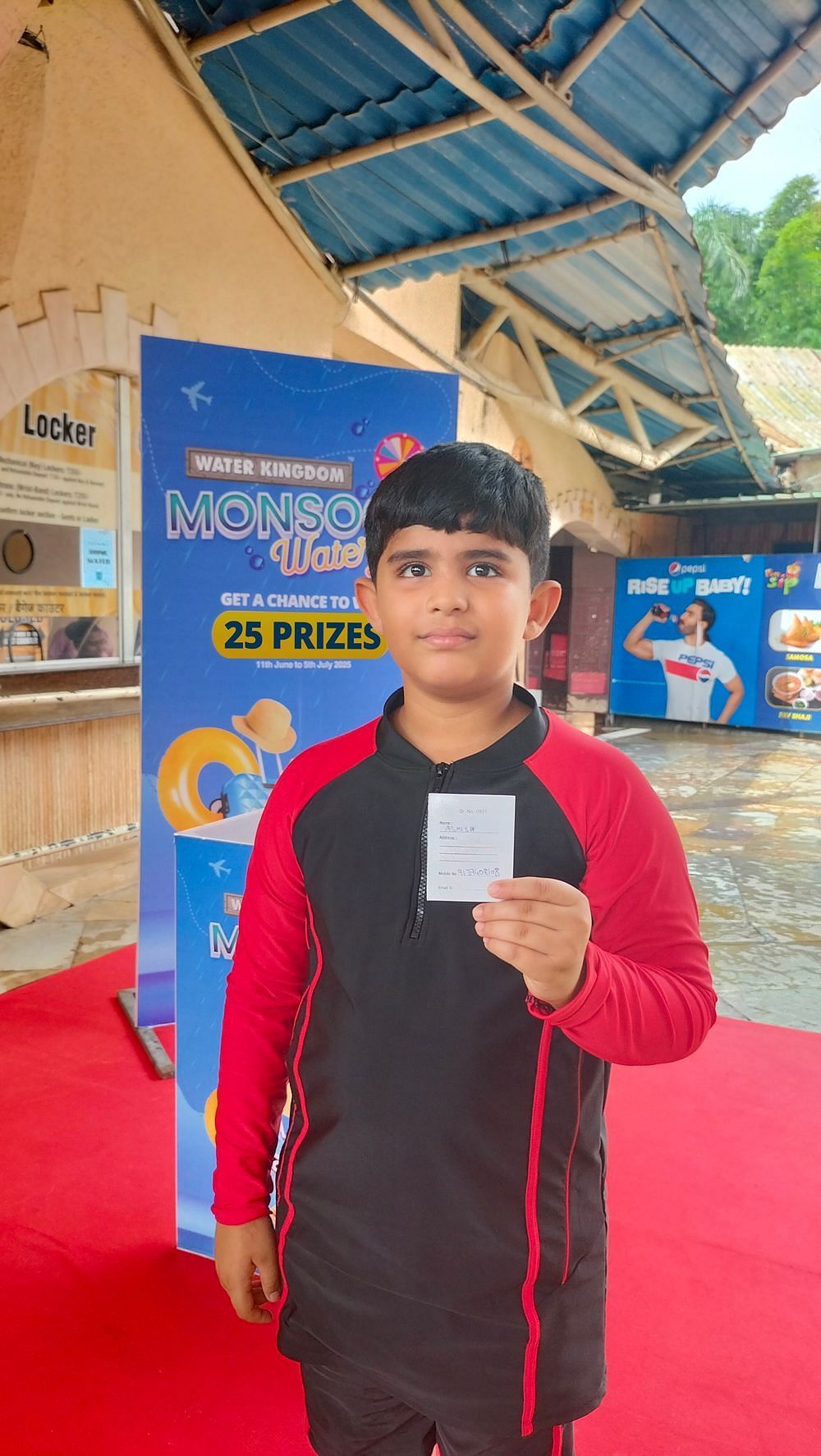  Water Kingdom Monsoon Waterfest winner holding a prize cup, standing near a colorful event banner with excitement