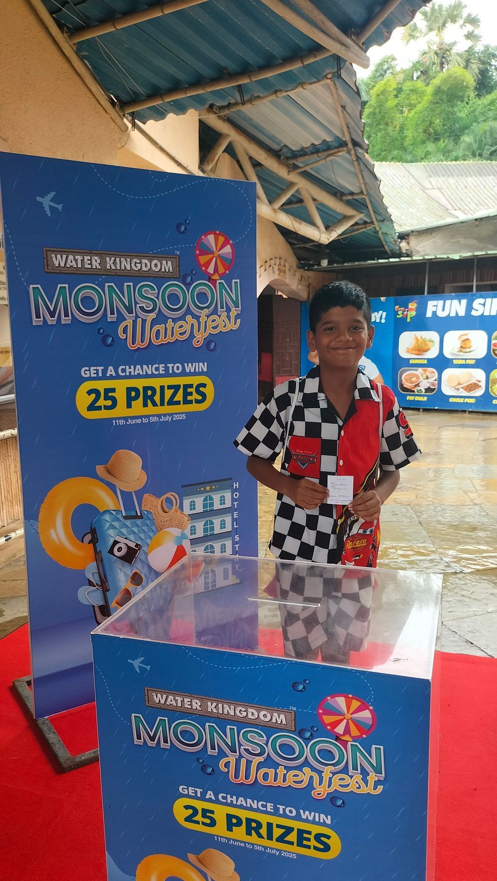 Water Kingdom Monsoon Waterfest winner holding their prize, standing proudly next to the event display banner.