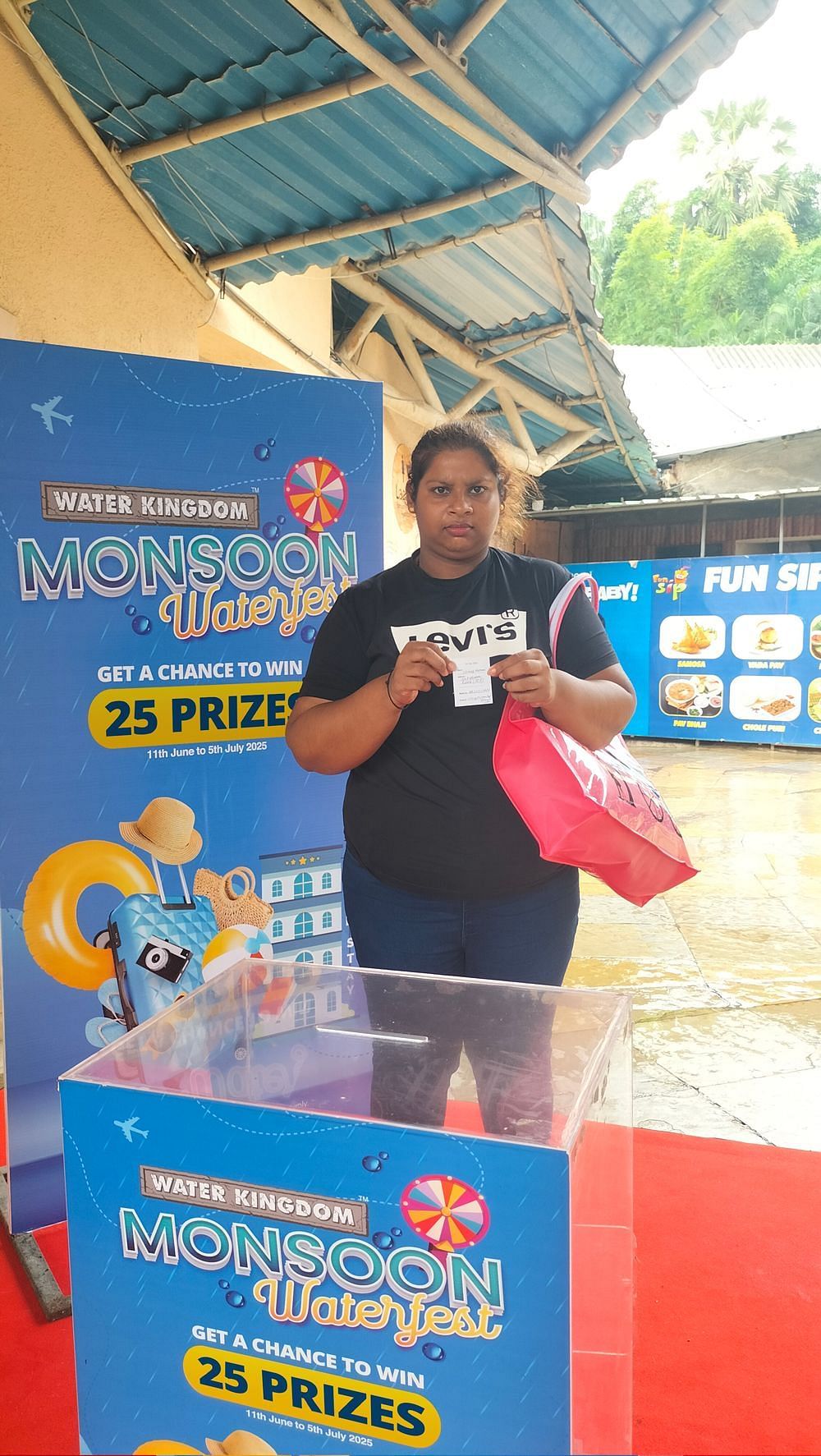Water Kingdom Monsoon Waterfest winner holding a mug in front of a vibrant event banner, beaming with joy