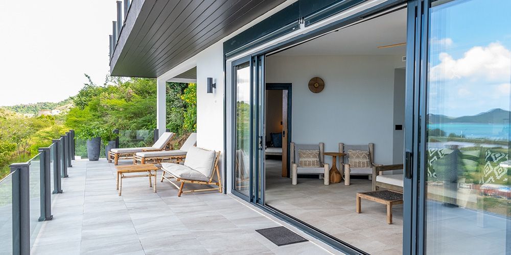 A modern house with large glass doors opening to an outdoor patio and lush green surroundings.