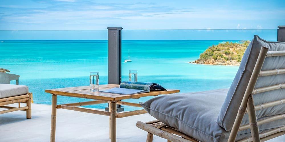 Private terrace with sun loungers and dining set overlooking the turquoise Caribbean Sea and a rocky islet
