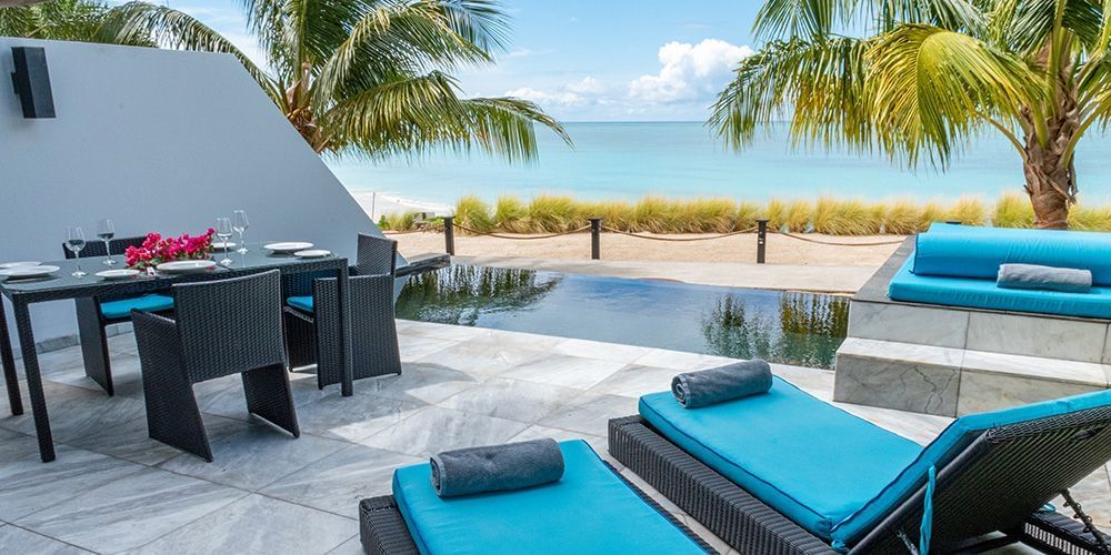 Outdoor lounge and dining area with blue sunbeds and ocean view at Tamarind Hills Resort and Villas - Antigua.