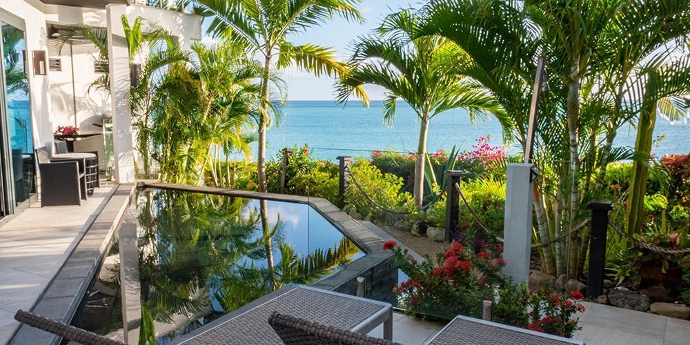  A resort villa with a private pool, surrounded by tropical foliage and palm trees, overlooking the ocean.