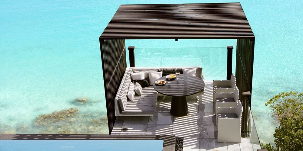  Overwater dining and lounge area with a thatched roof, surrounded by calm ocean and coral formations.