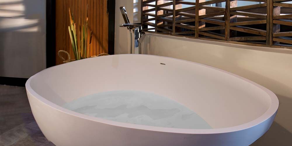 Oval bathtub filled with water, placed in a bathroom with warm lighting and wooden accents.