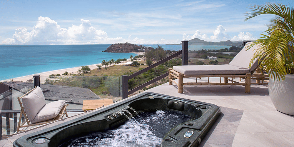 An outdoor terrace with a hot tub and lounge chairs, providing a stunning elevated view of the ocean and coastline.