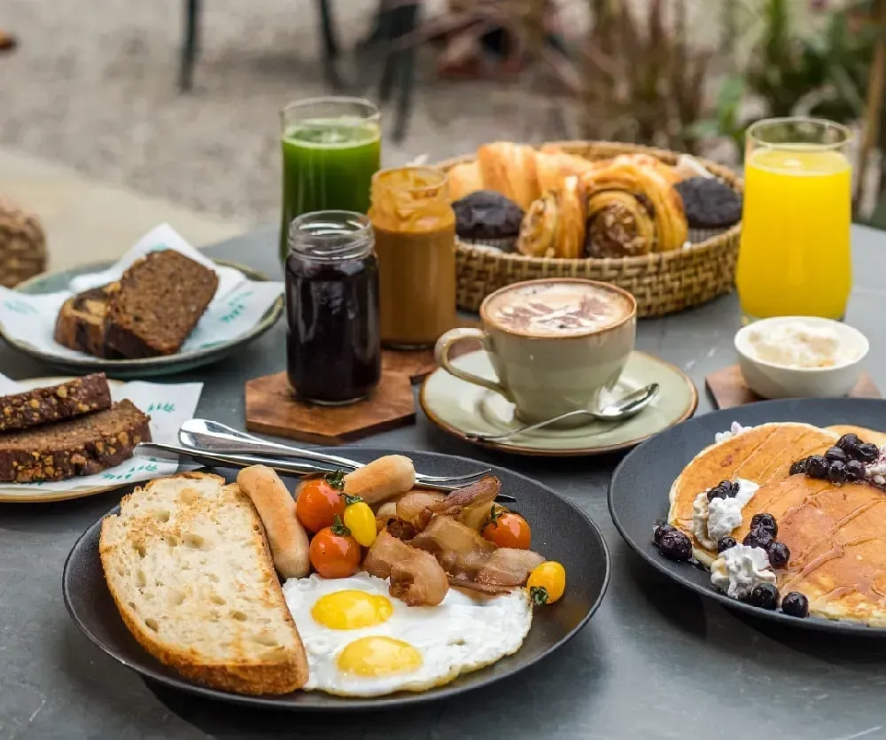 Breakfast spread at Karma Chalets featuring eggs, bread, fruits, pastries, and juices on an outdoor table.