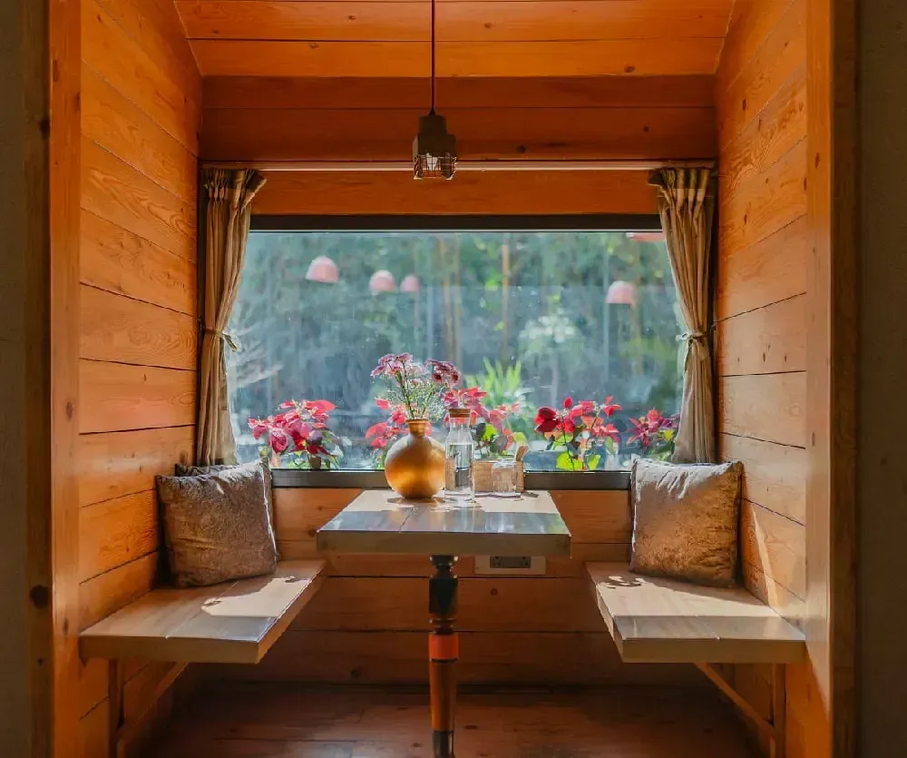 Wooden cabin-style dining area at Karma Chalets with a central table and large window view of the forest.