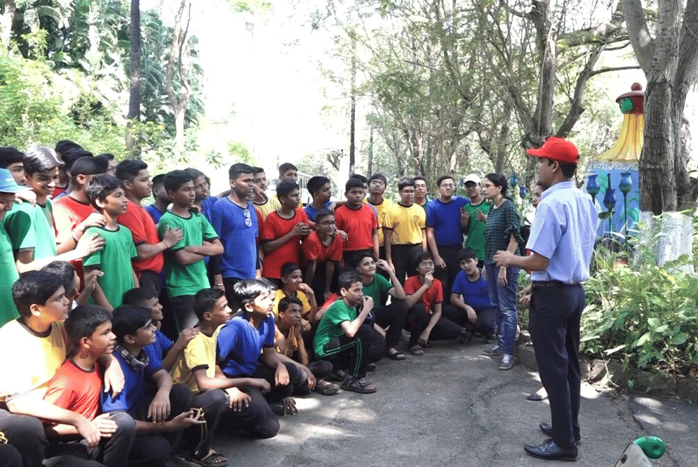 A group of students gathered around an instructor wearing a red cap during an outdoor guided session at Water Kingdom.