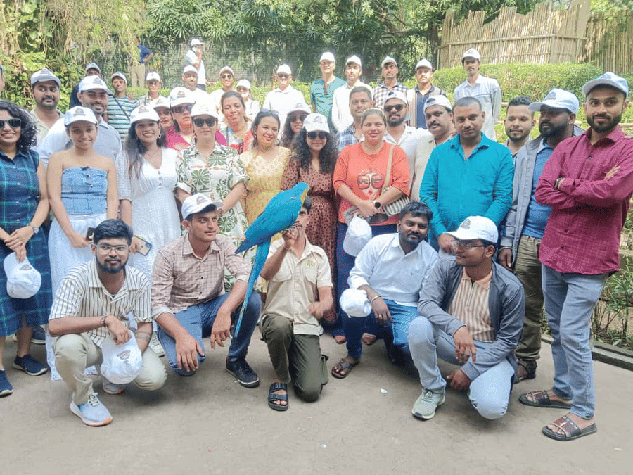A large group of visitors posing together at EsselWorld Bird Park, Mumbai, with a vibrant blue macaw perched at the front; people are smiling and enjoying the outdoor greenery.