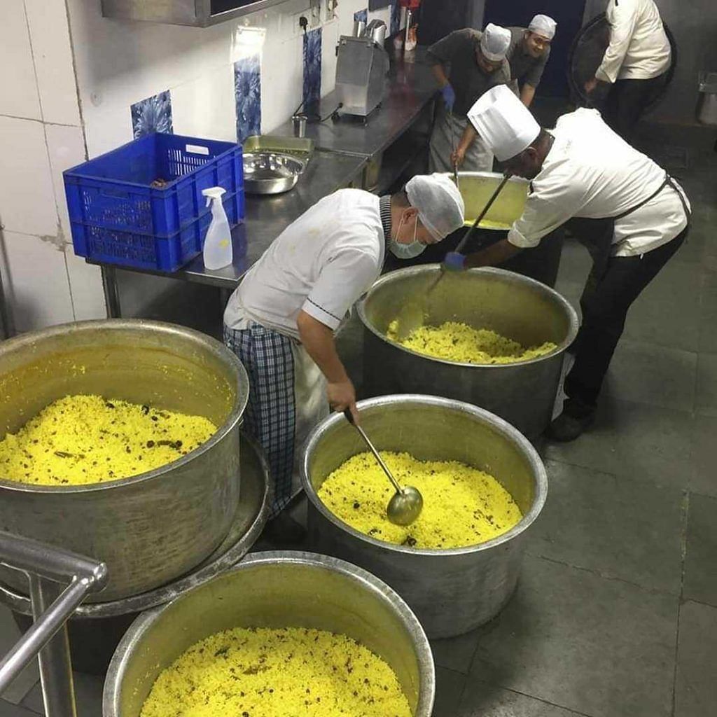 Multiple chefs cooking food in the kitchen in big containers.