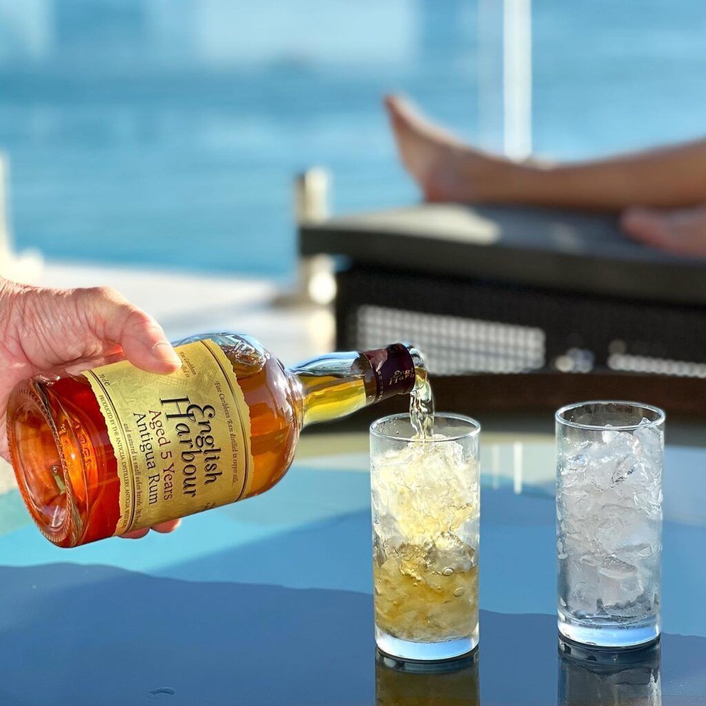 A hand pouring drinks into one of two glasses placed on a glass table.
