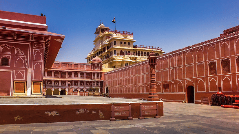 A grand palace courtyard is enclosed by terracotta-pink walls, with a multi-storey yellow tower rising behind.