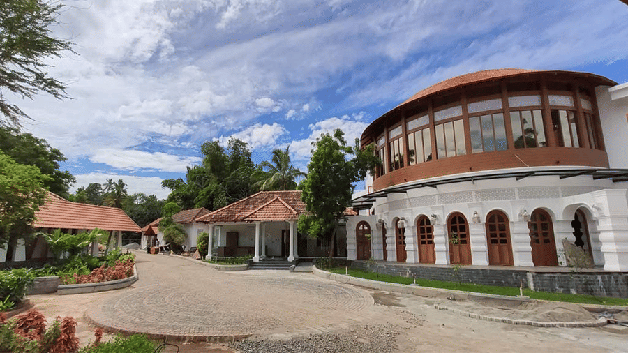A large circular building with tall arches and a curved facade, surrounded by greenery under a blue sky.