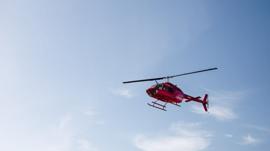 A red helicopter up in the air on a sunny day.