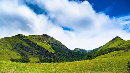 Scenic view of lush green hills under a bright blue sky with clouds