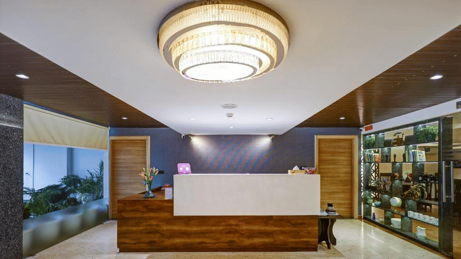 The reception area at Hotel 91 HUDA Premier, Gurugram with a front desk, ceiling light, shelves, glass partitions, and seating space.