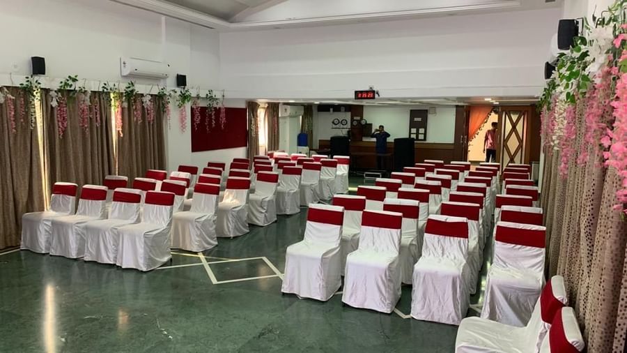 Spacious banquet hall with seating arranged for a seminar or celebration, featuring white chair covers and maroon sashes.