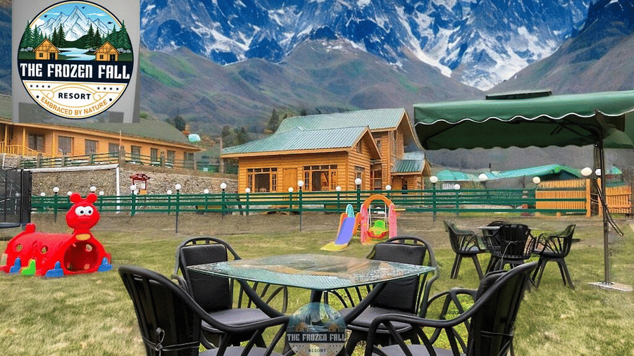 An outdoor dining area at Dawat e Drung by FrozenFall Resort, Drung, Tangmarg, featuring lawn seating, play slides and a snow-capped mountain backdrop.